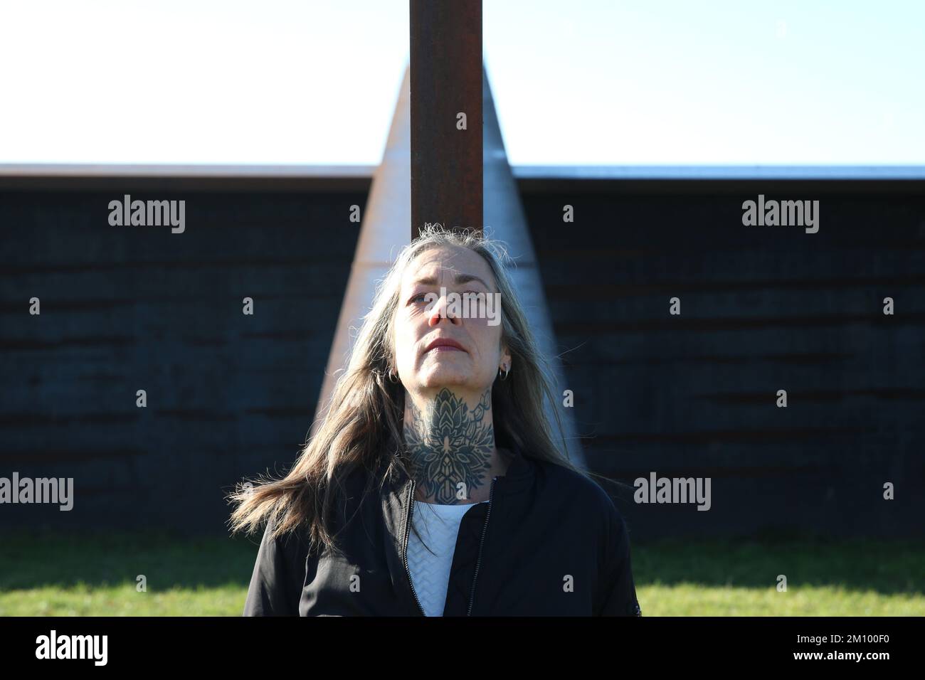 Best Ager Female Model in front of metal wall looking up and enjoy the sun. Frau im besten Alter blickt nach oben und genießt die Sonne. 50+, Tattoo Stock Photo