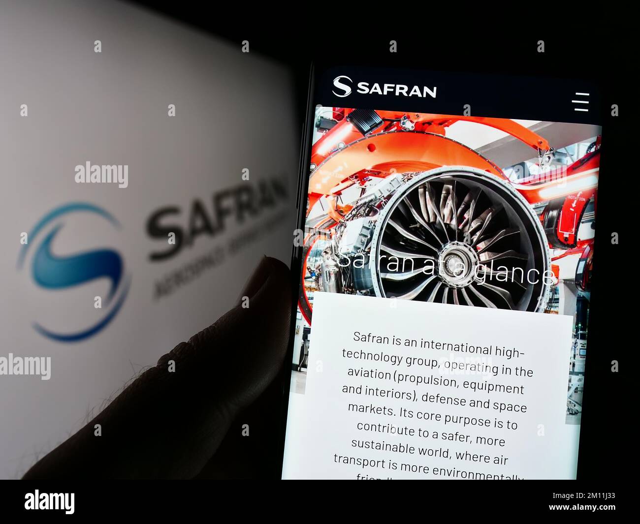 Person holding smartphone with website of French aerospace company Safran S.A. on screen in front of logo. Focus on center of phone display. Stock Photo