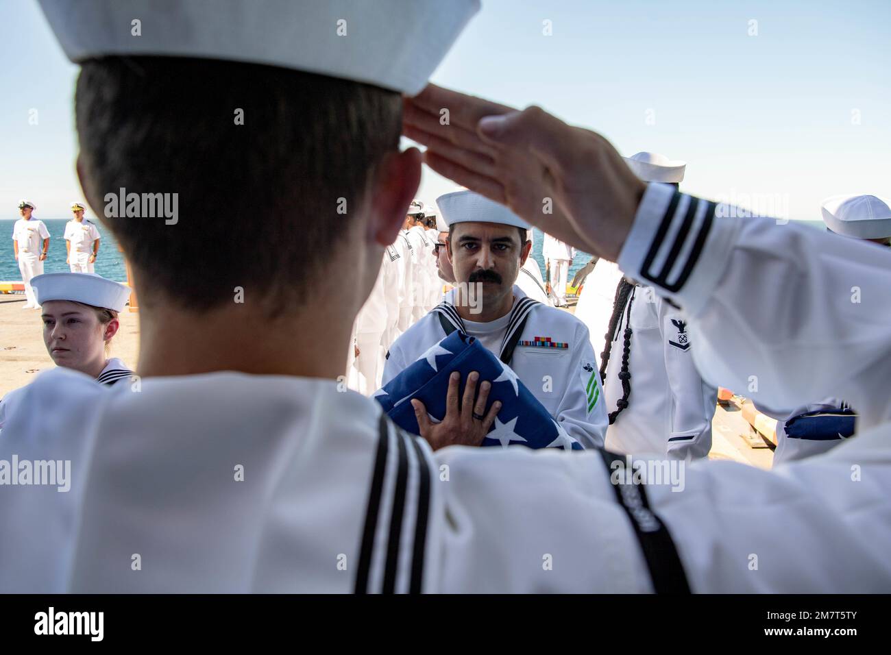 PACIFIC OCEAN (May 12, 2022) Airman Lincoln Shirah, a native of Metamora, Michigan, salutes the national ensign carried by Air Traffic Controlman Airman Cody Moore, a native of Atascadero, California, during a burial at sea aboard amphibious assault ship USS Essex (LHD 2), May 12, 2022. Essex is underway conducting routine operations in U.S. 3rd Fleet. Stock Photo