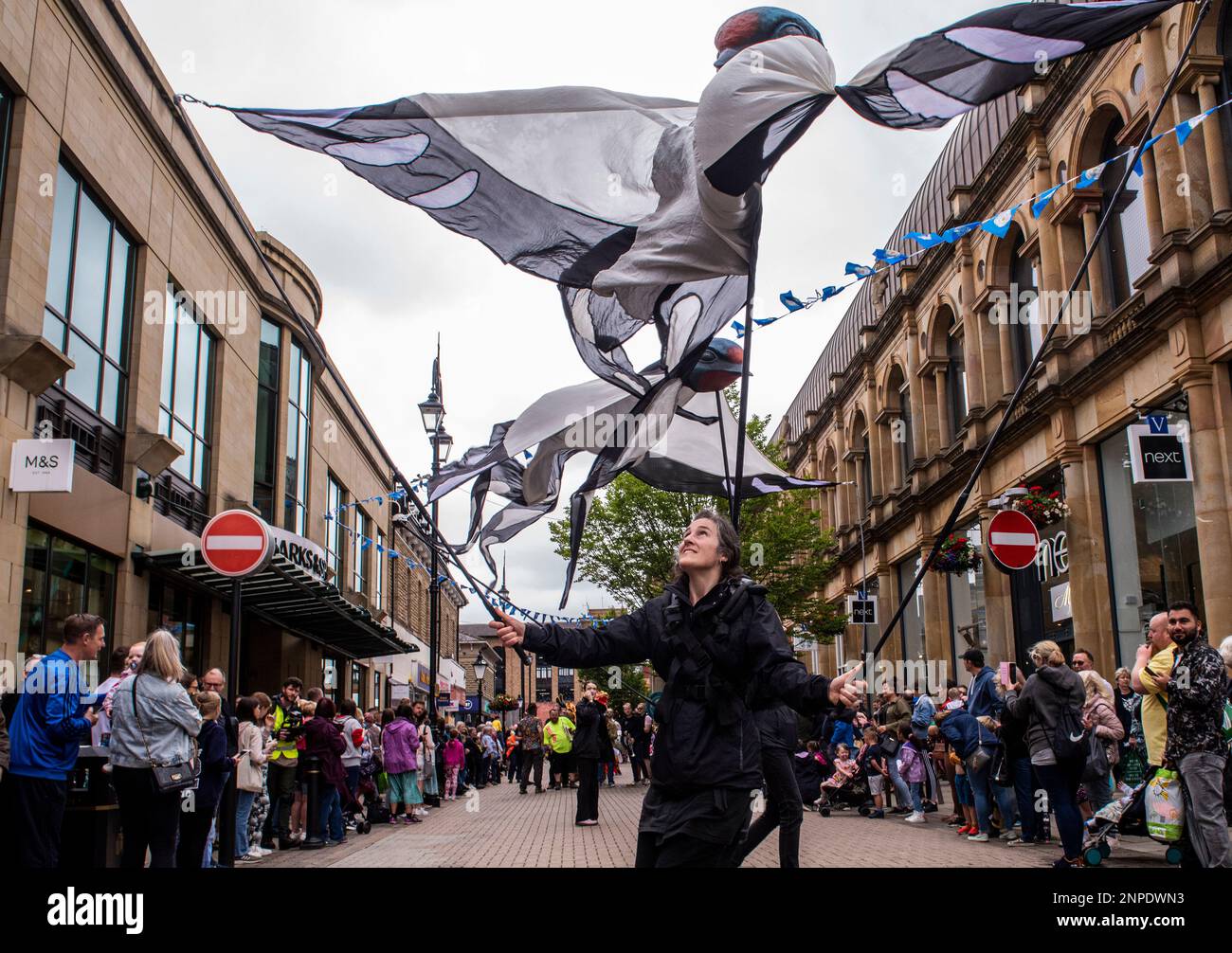 A street artist parades among the overlooking crowd while controlling a huge fabric bird using long sticks. Stock Photo