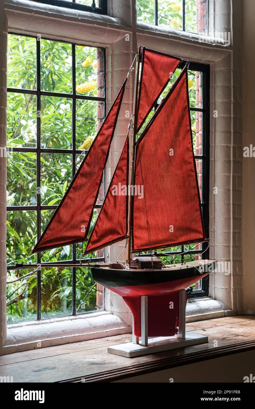 Model boat with red sails in window of Wiveton Hall, a 17th century Jacobean manor house in Norfolk, UK Stock Photo