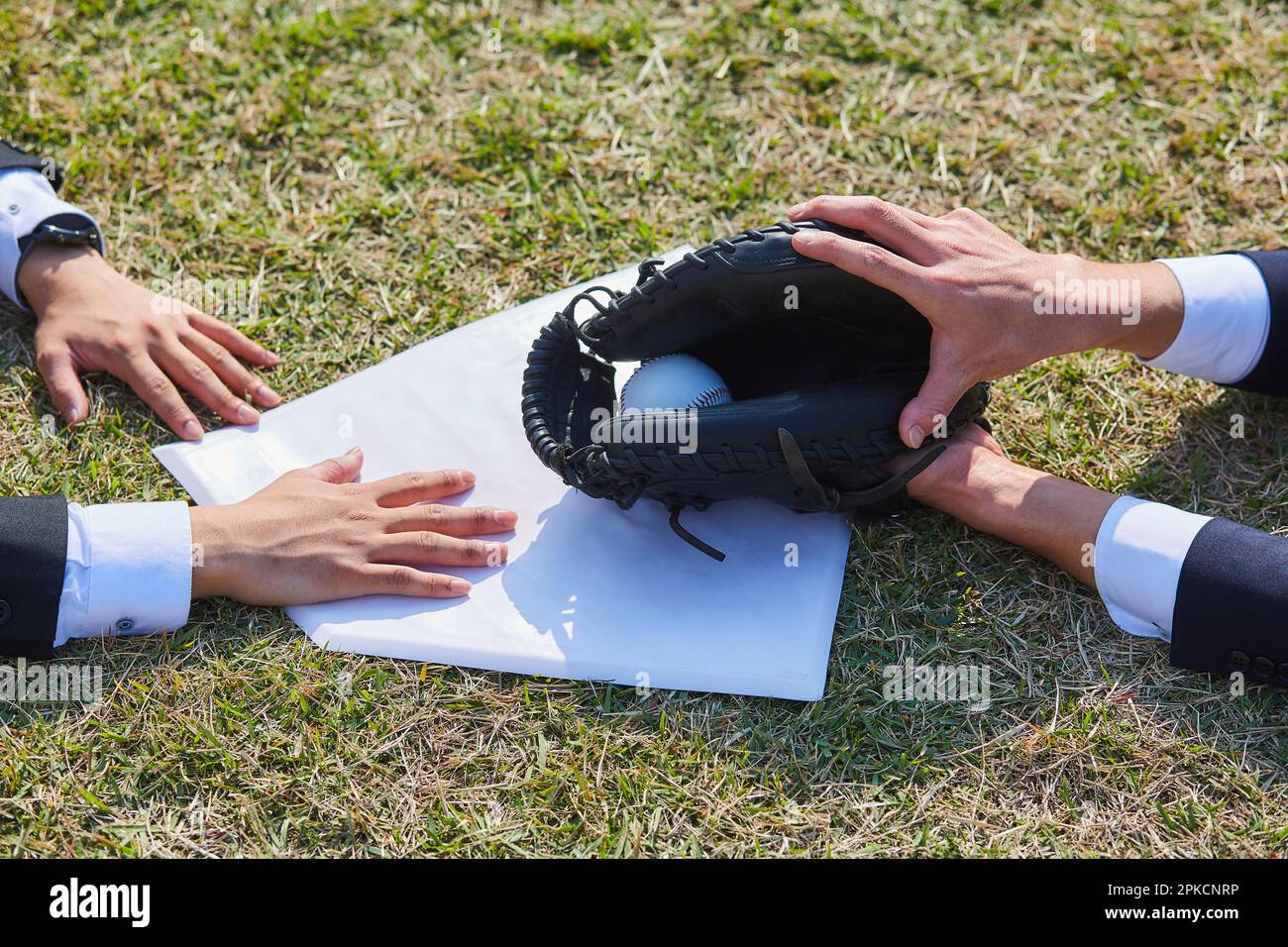 Hands of two men in suits sliding into home base Stock Photo