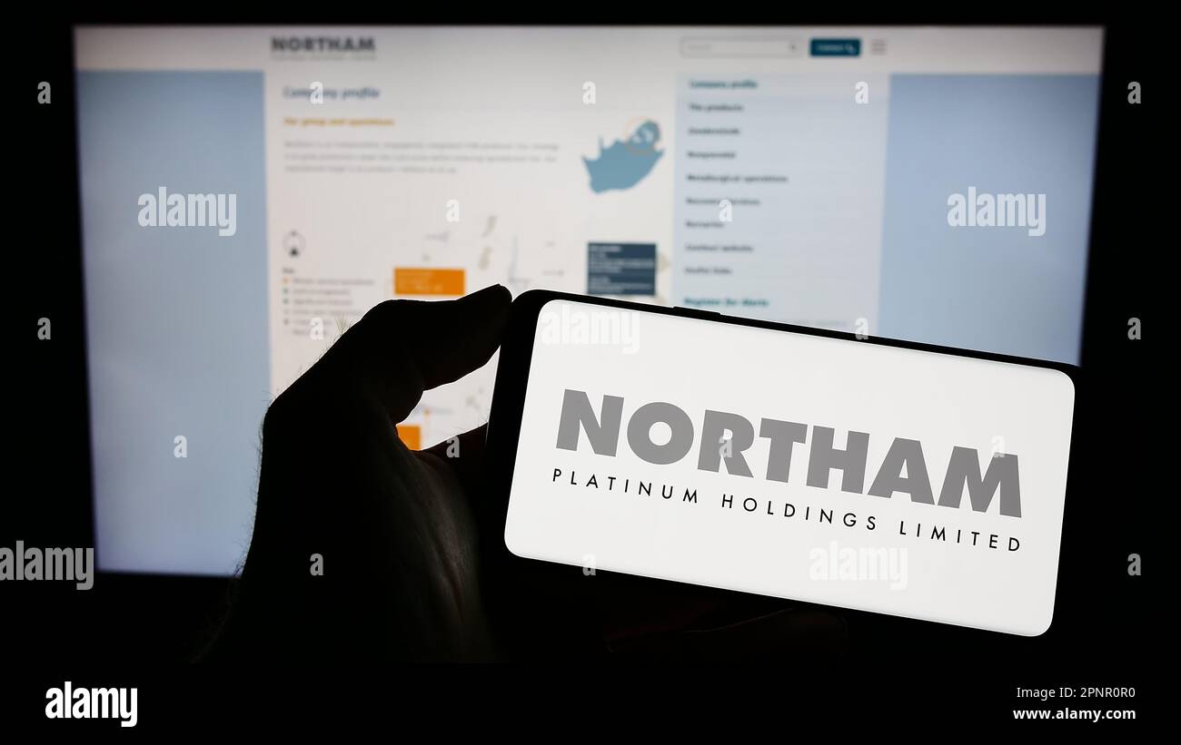 Person holding mobile phone with logo of company Northam Platinum Holdings Limited on screen in front of web page. Focus on phone display. Stock Photo