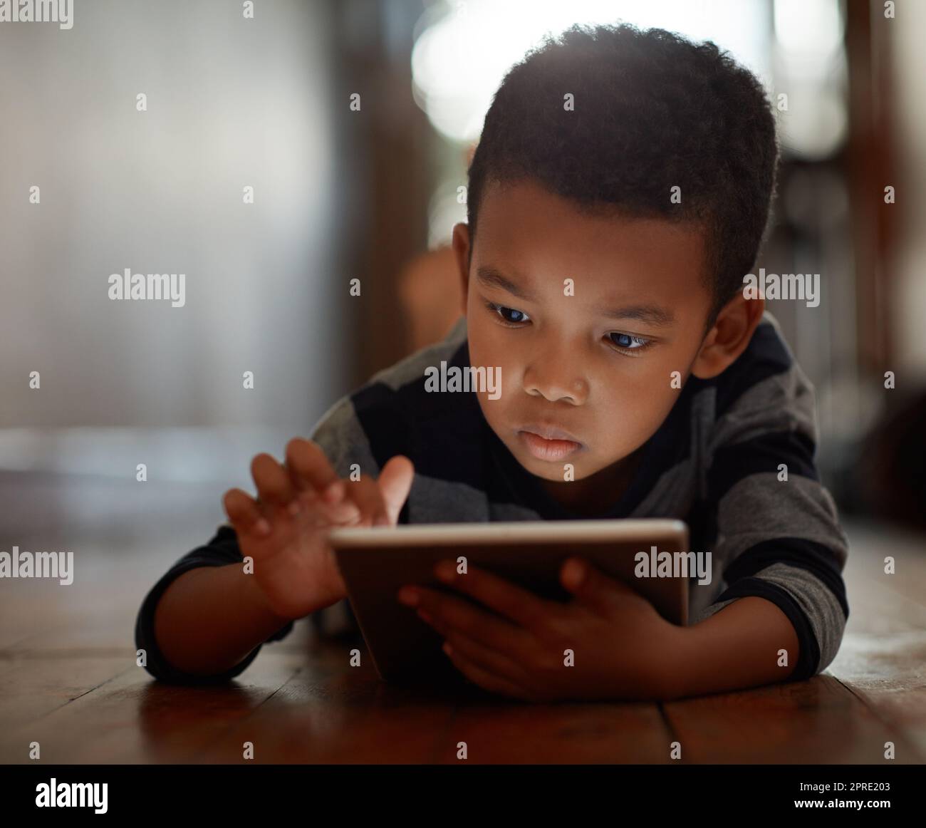 Exploring a world of apps. a young boy using his digital tablet while lying on the floor at home. Stock Photo