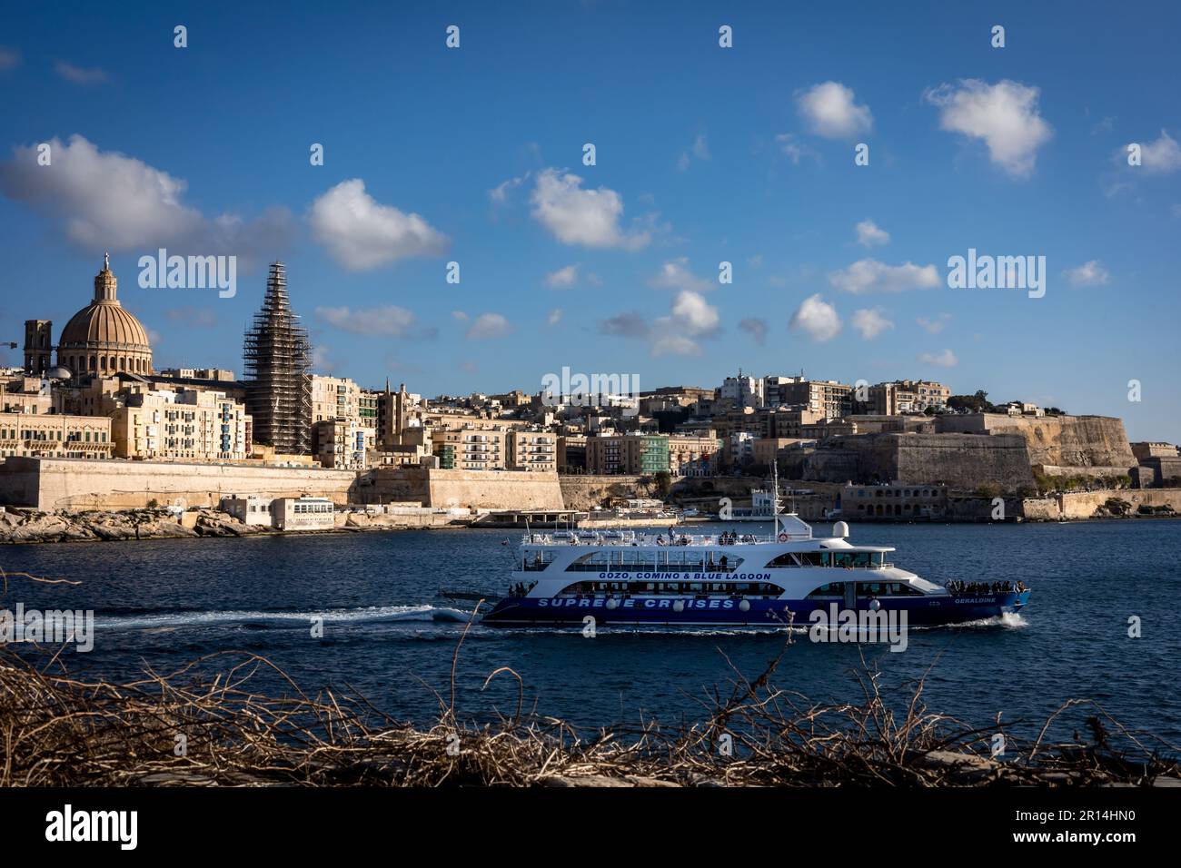 Valletta, Malta - April 18, 2023: A panorama of old town Valletta, viewed from Sliema. Tourist cruise boat in foreground. Stock Photo