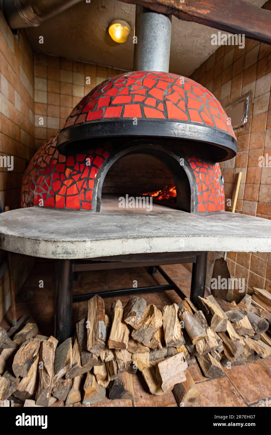 An interior shot of a rustic wood fired oven with a pile of logs beside it in a traditional stone building Stock Photo