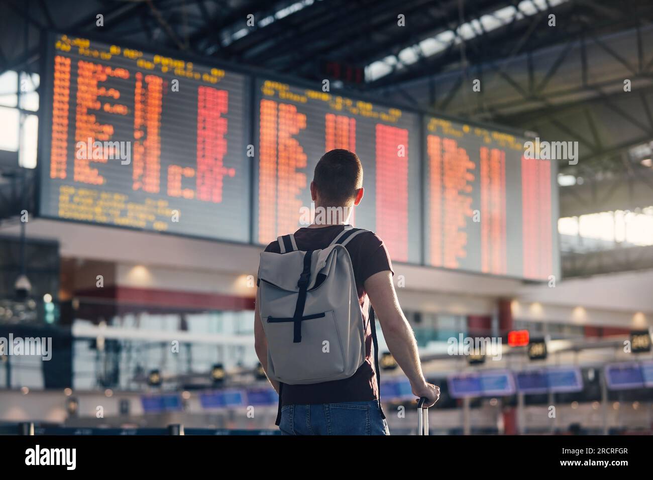 Traveling by airplane. Man walking with backpack and suitcase walking through airport terminal and looking at departure information. Stock Photo