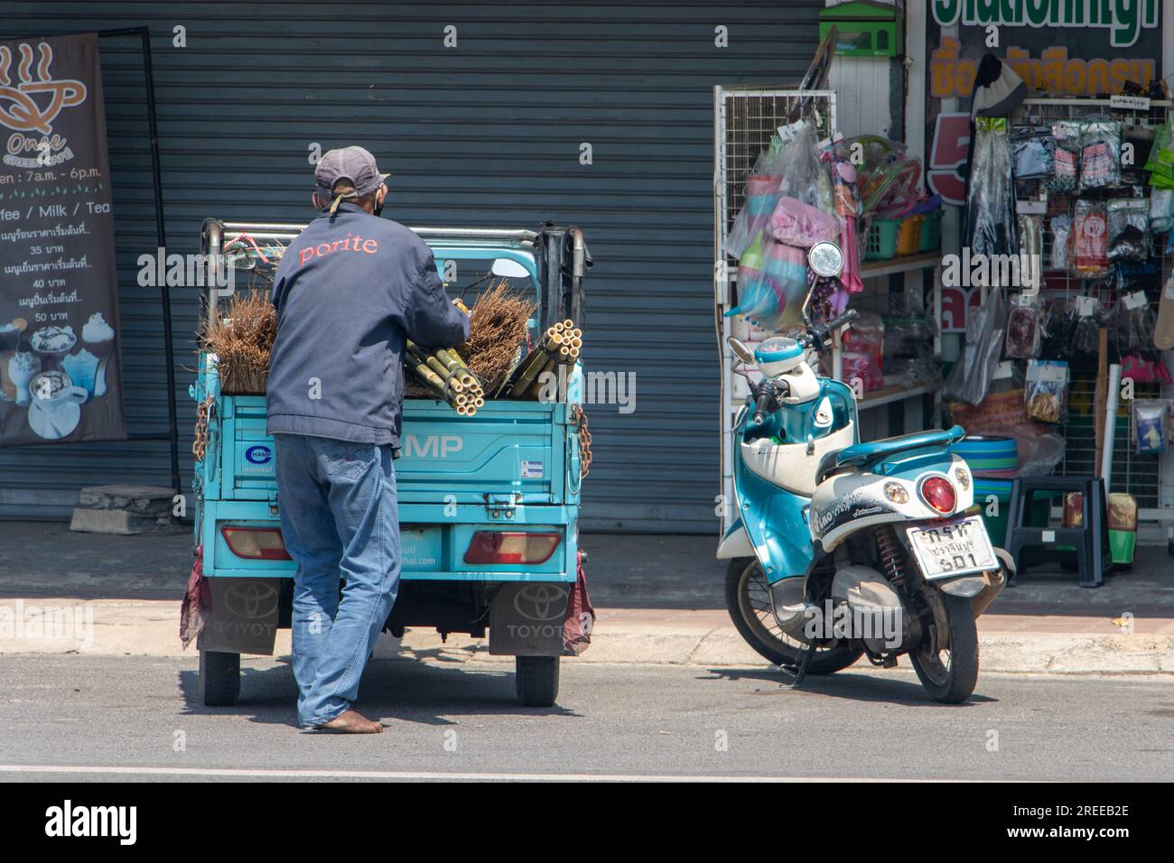 PRACHIN BURI, THAILAND, FEB 26 2023, A man unloads a load of handmade brooms from a small truck Stock Photo