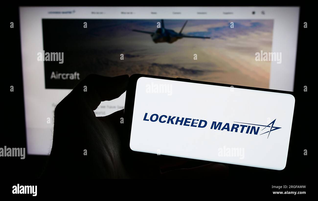 Person holding smartphone with logo of US defense company Lockheed Martin Corporation on screen in front of website. Focus on phone display. Stock Photo