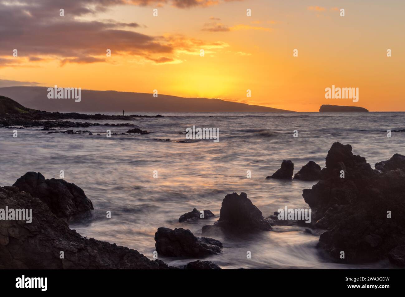 A vibrant sunset cloaks Maluaka Beach, with the silhouette of Molokini Crater on the horizon. Stock Photo