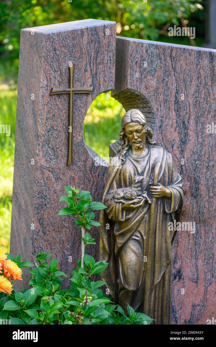 Decorated grave with a gravestone with cross and 'The Good Shepherd' figure Stock Photo