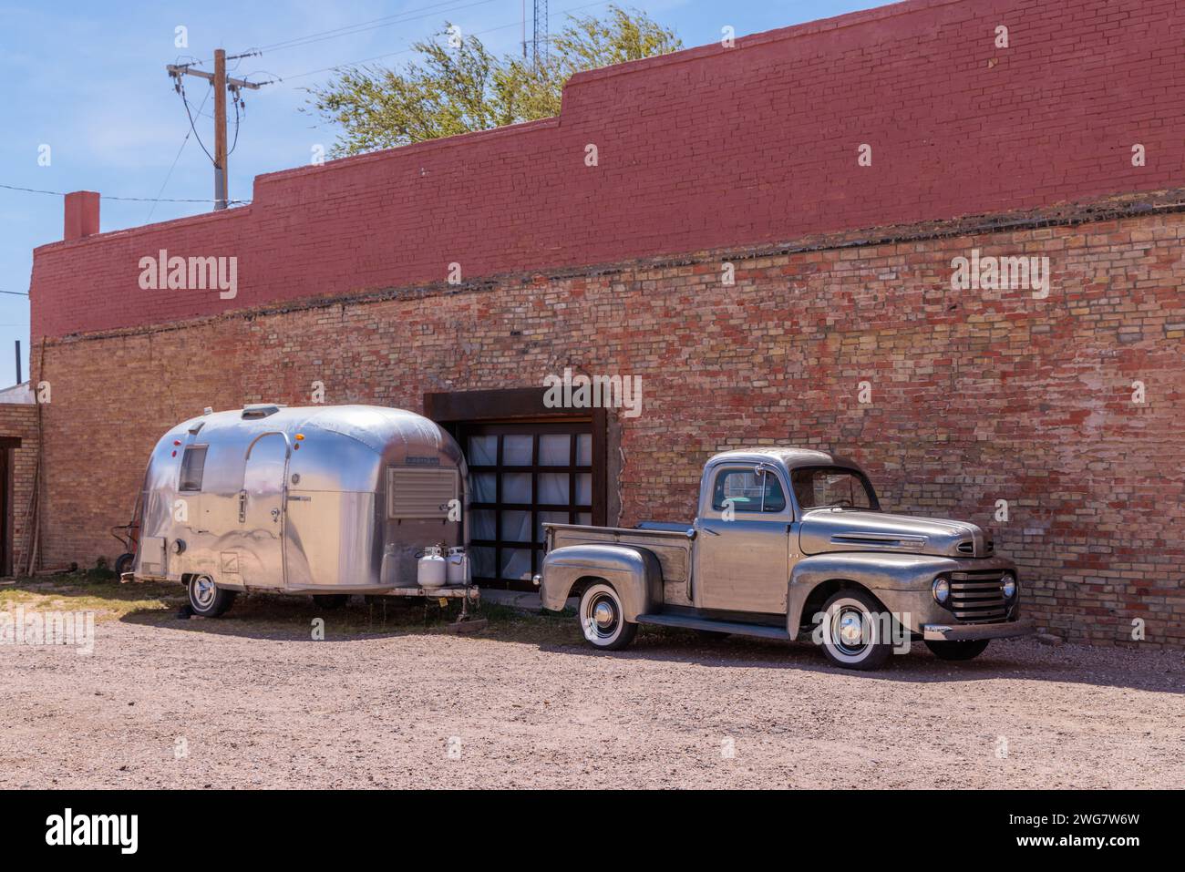 Silver painted classic fort pickup truck and a stainless steel Airstream camper travel trailer parked in downtown Winslow Arizona Stock Photo