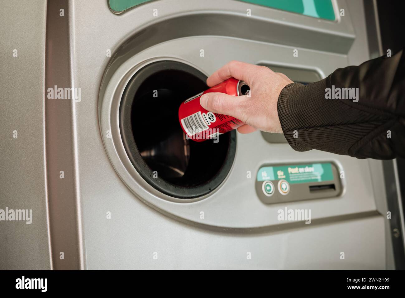 Returning empty bottles and cans in the recycling machine at the supermarket to reduce waste and reuse plastic, glass and aluminum. Hand holding a can Stock Photo