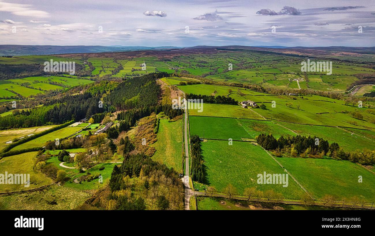 Aerial view of a lush green landscape with fields, trees, and a long road stretching across the scene under a partly cloudy sky. Stock Photo