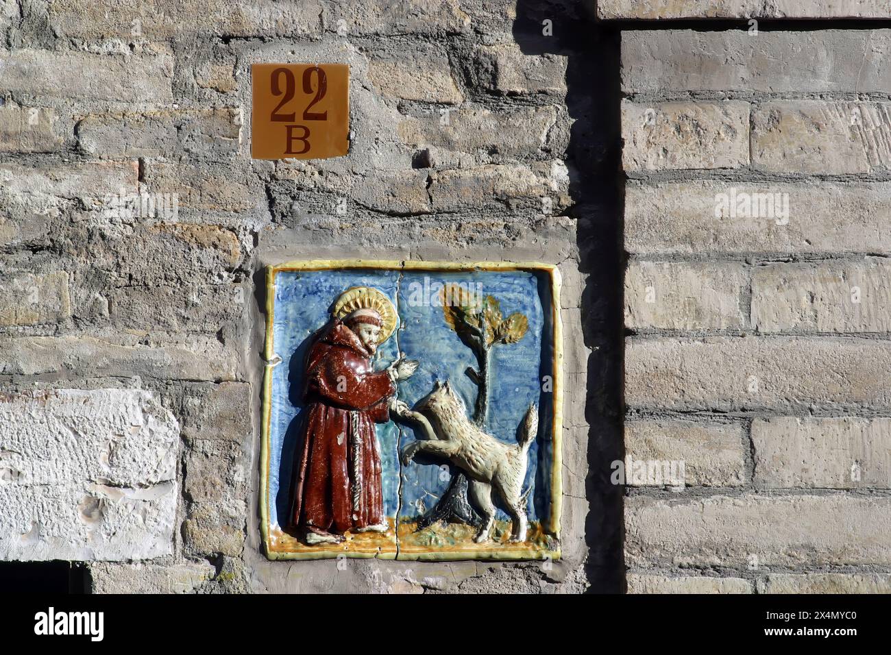 Ceramic tile set into a wall showing Saint Francis befriending a wolf, Assisi, Umbria, Italy Stock Photo