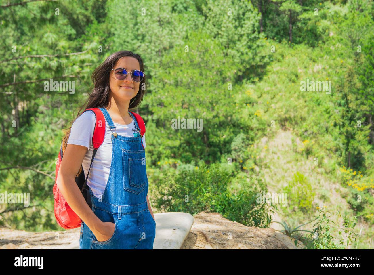 young traveler looking happy and with a positive attitude towards the front, dressed in jeans overalls and a white shirt. Stock Photo