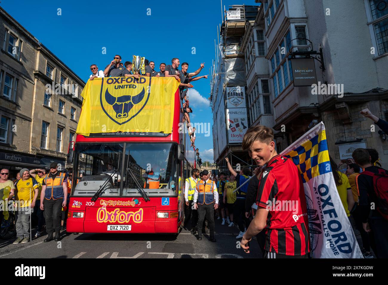 Thousands of Oxford United fans lined the city centre of Oxford to celebrate the promotion of Oxford United to the EFL Championship after beating the Bolton Wanders in the League One playoff at Wembley on the weekend. The crowds, decked out in yellow, cheered loudly and let off yellow flares as the open-top bus carrying the team and staff slowly moved along the High Street to the Oxford City Town Hall, where they attended an invite-only civic reception. The Oxford United flag flew over the Oxford City Council building in celebration. Stock Photo