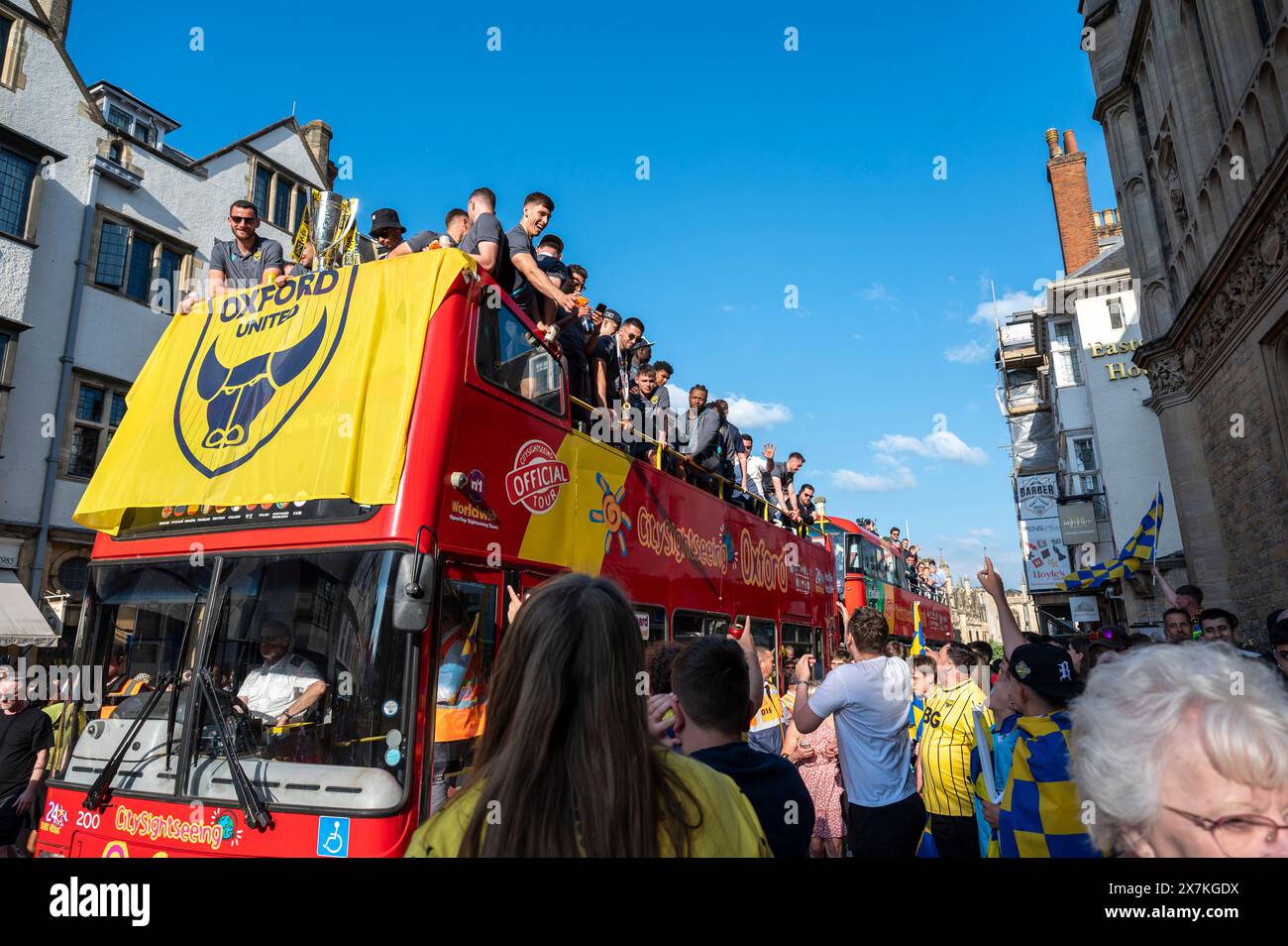 Thousands of Oxford United fans lined the city centre of Oxford to celebrate the promotion of Oxford United to the EFL Championship after beating the Bolton Wanders in the League One playoff at Wembley on the weekend. The crowds, decked out in yellow, cheered loudly and let off yellow flares as the open-top bus carrying the team and staff slowly moved along the High Street to the Oxford City Town Hall, where they attended an invite-only civic reception. The Oxford United flag flew over the Oxford City Council building in celebration. Stock Photo