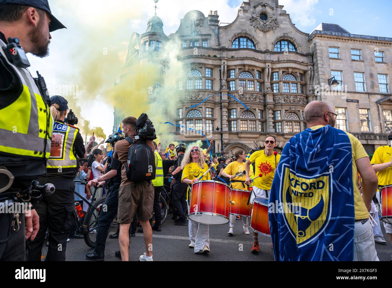 Thousands of Oxford United fans lined the city centre of Oxford to celebrate the promotion of Oxford United to the EFL Championship after beating the Bolton Wanders in the League One playoff at Wembley on the weekend. The crowds, decked out in yellow, cheered loudly and let off yellow flares as the open-top bus carrying the team and staff slowly moved along the High Street to the Oxford City Town Hall, where they attended an invite-only civic reception. The Oxford United flag flew over the Oxford City Council building in celebration. Stock Photo