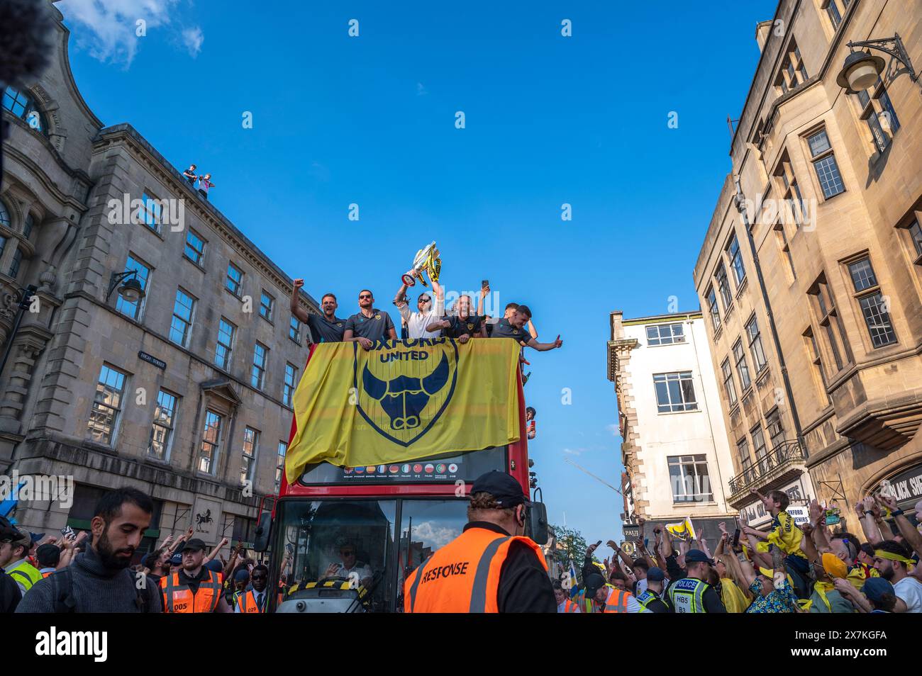 Thousands of Oxford United fans lined the city centre of Oxford to celebrate the promotion of Oxford United to the EFL Championship after beating the Bolton Wanders in the League One playoff at Wembley on the weekend. The crowds, decked out in yellow, cheered loudly and let off yellow flares as the open-top bus carrying the team and staff slowly moved along the High Street to the Oxford City Town Hall, where they attended an invite-only civic reception. The Oxford United flag flew over the Oxford City Council building in celebration. Stock Photo