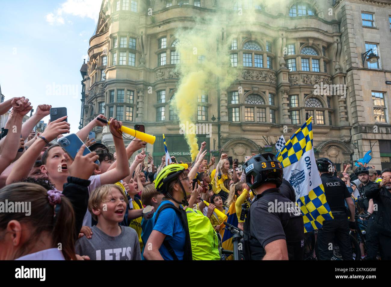 Thousands of Oxford United fans lined the city centre of Oxford to celebrate the promotion of Oxford United to the EFL Championship after beating the Bolton Wanders in the League One playoff at Wembley on the weekend. The crowds, decked out in yellow, cheered loudly and let off yellow flares as the open-top bus carrying the team and staff slowly moved along the High Street to the Oxford City Town Hall, where they attended an invite-only civic reception. The Oxford United flag flew over the Oxford City Council building in celebration. Stock Photo