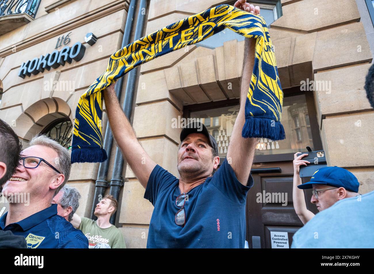 Thousands of Oxford United fans lined the city centre of Oxford to celebrate the promotion of Oxford United to the EFL Championship after beating the Bolton Wanders in the League One playoff at Wembley on the weekend. The crowds, decked out in yellow, cheered loudly and let off yellow flares as the open-top bus carrying the team and staff slowly moved along the High Street to the Oxford City Town Hall, where they attended an invite-only civic reception. The Oxford United flag flew over the Oxford City Council building in celebration. Stock Photo