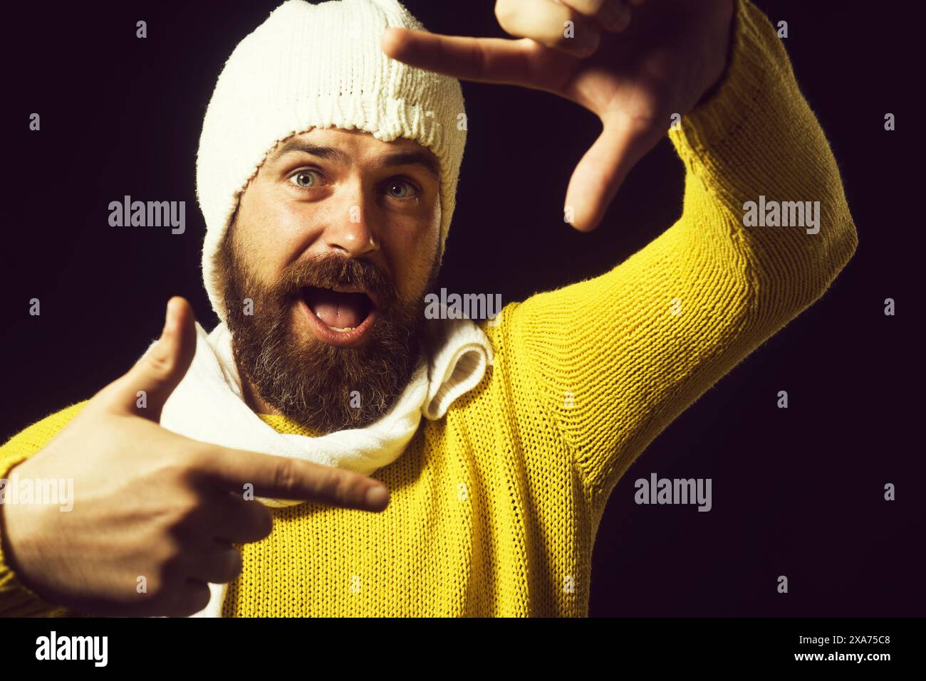 Funny bearded framing face with hands. Happy man creating frame with fingers. Imaginary selfie photo. Handsome guy in yellow sweater, white hat and sc Stock Photo