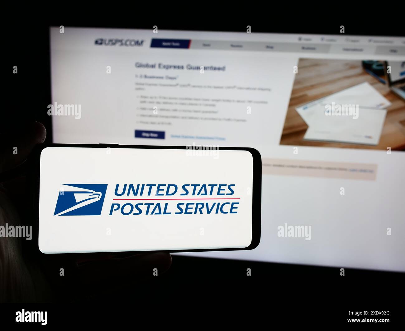 Person holding smartphone with logo of US agency United States Postal Service (USPS) in front of website. Focus on phone display. Stock Photo