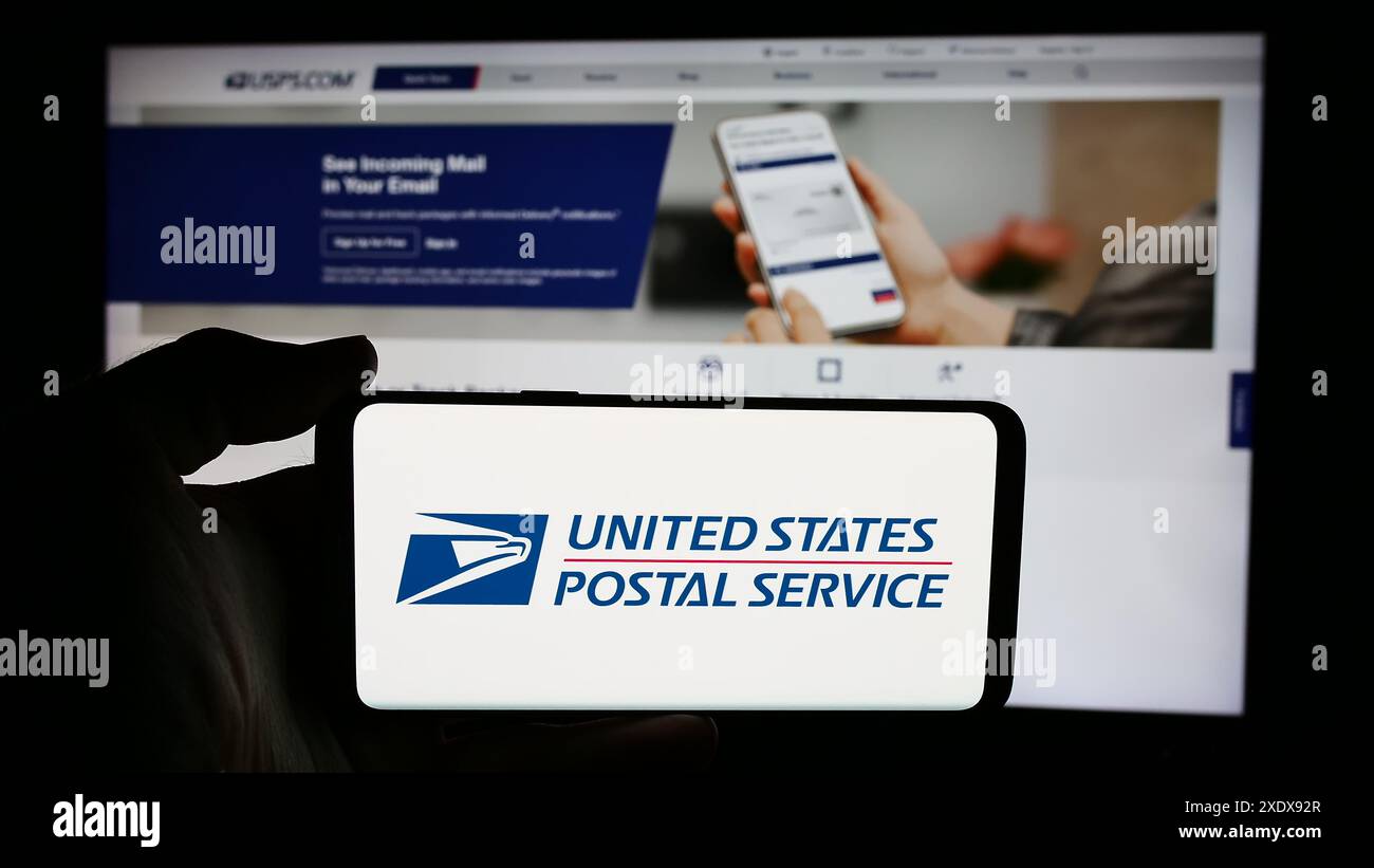 Person holding cellphone with logo of US agency United States Postal Service (USPS) in front of webpage. Focus on phone display. Stock Photo