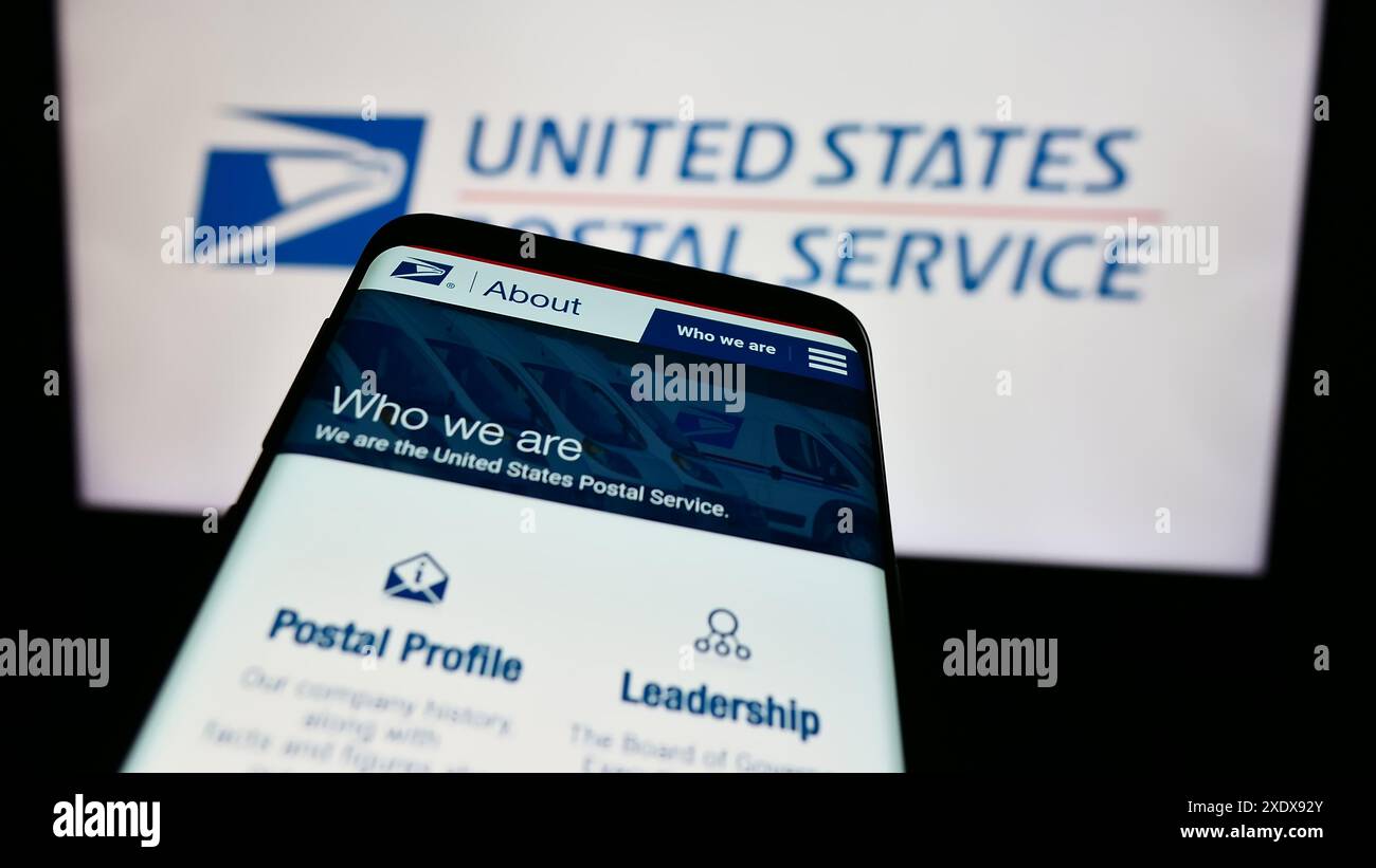 Mobile phone with website of US agency United States Postal Service (USPS) in front of logo. Focus on top-left of phone display. Stock Photo