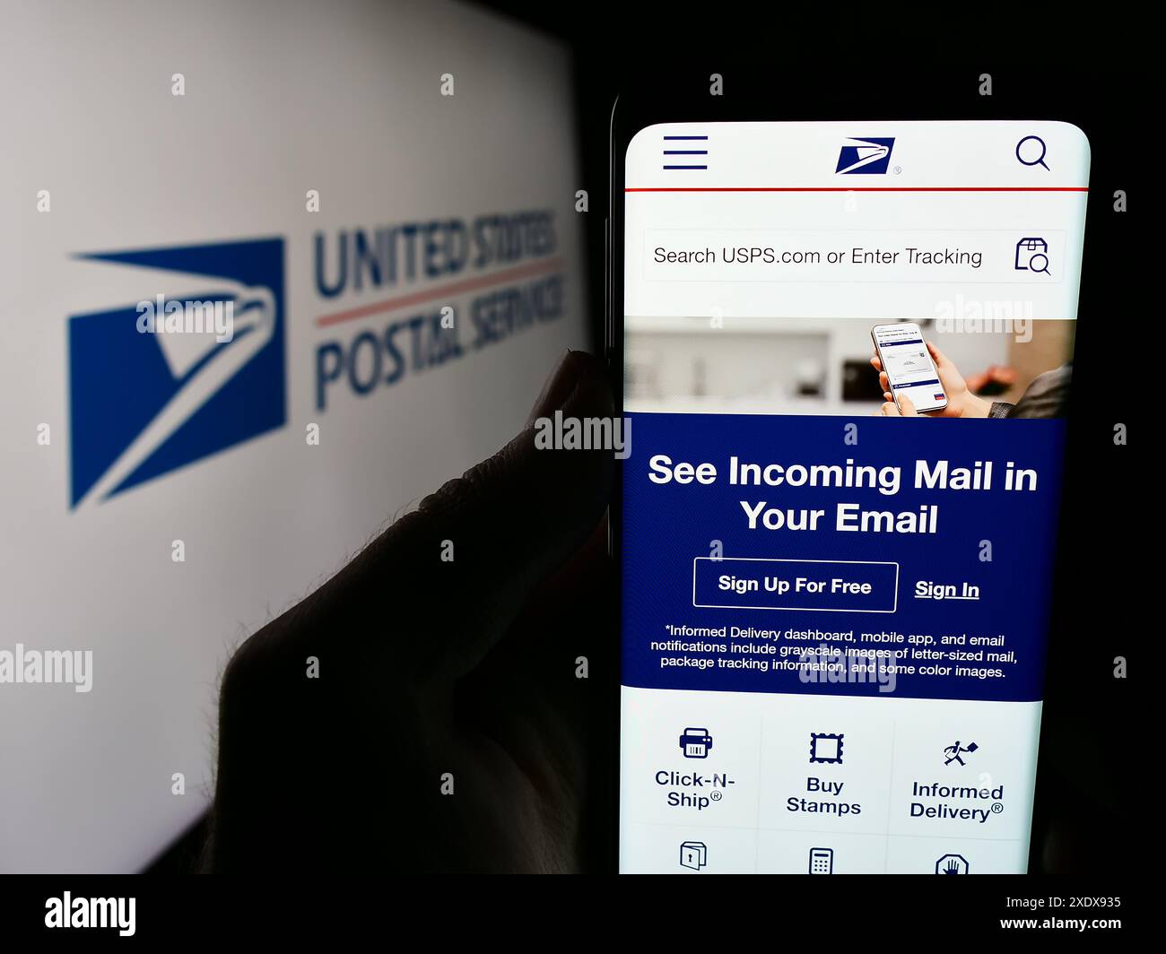 Person holding smartphone with webpage of US agency United States Postal Service (USPS) in front of logo. Focus on center of phone display. Stock Photo