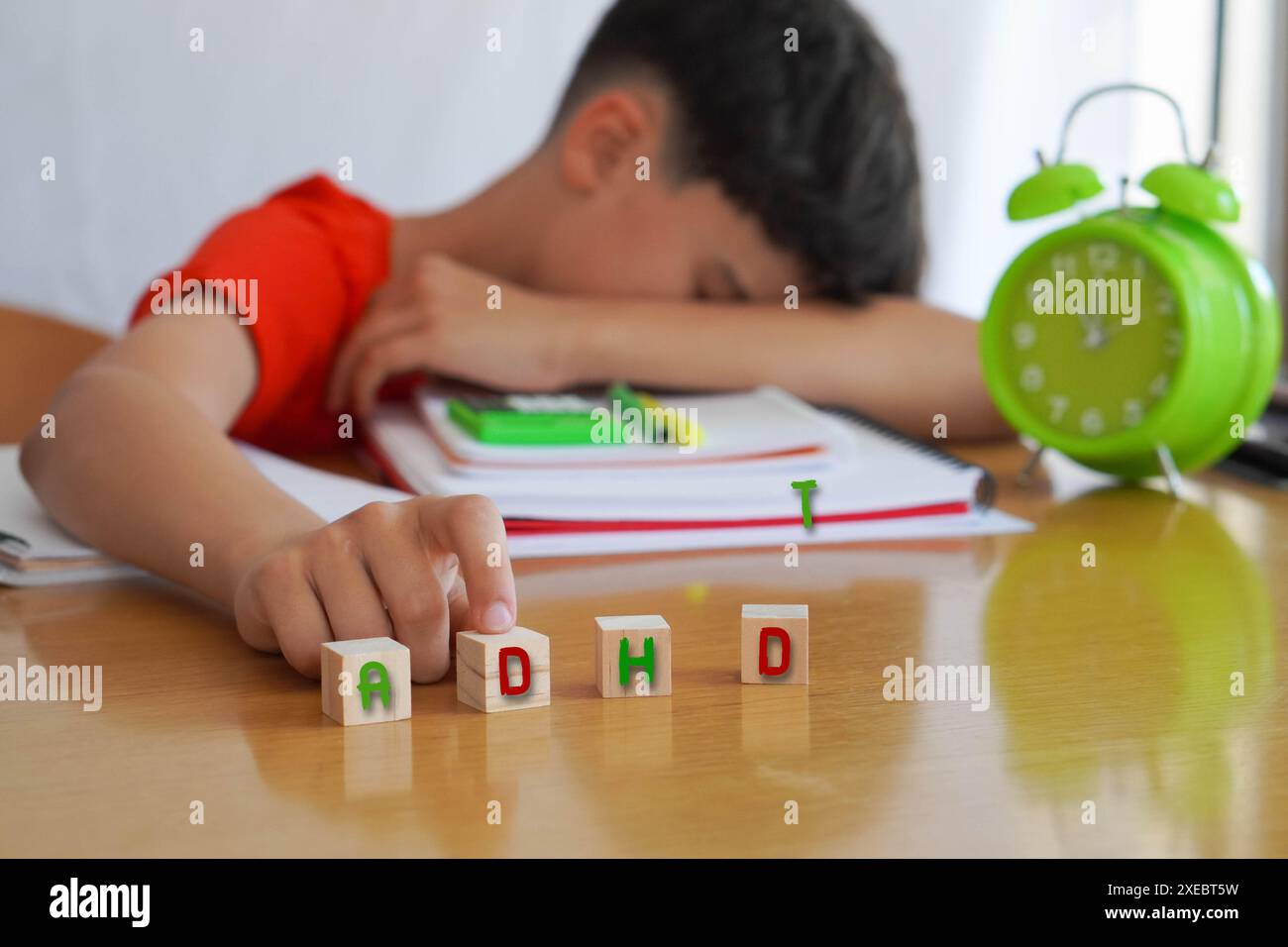 child surrounded by books and notebooks frustrated, with the acronym ADHD, represents the disease Attention Deficit Disorder and the difficulties it e Stock Photo