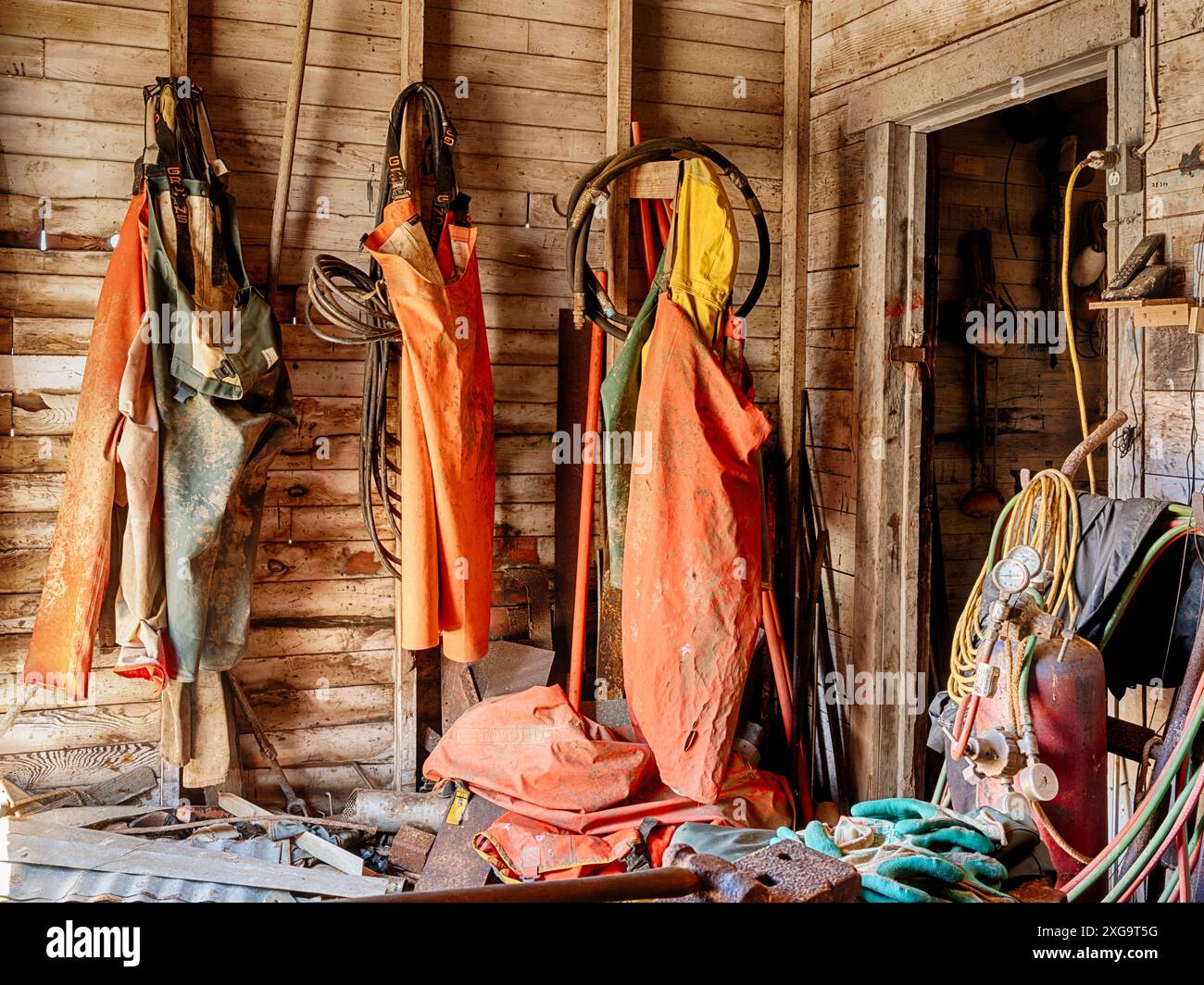 A group of three sets of overalls are hanging from hooks on the wall in the net shed at an oyster farm on Wallowa Bay in Washington. Stock Photo