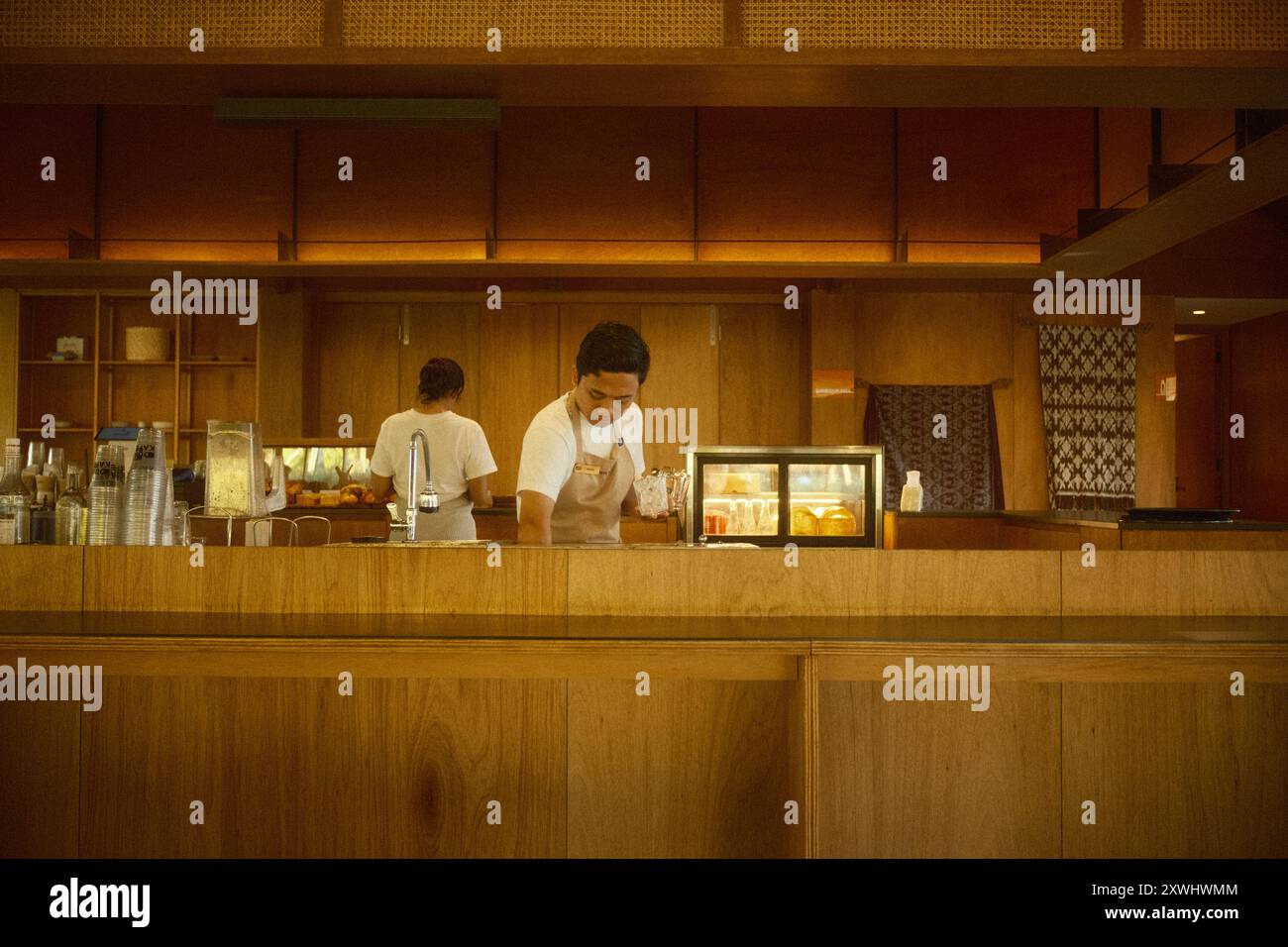 Nusa Dua, Bali, Indonesia - August 19, 2024: Two cafe workers are preparing orders at a coffee and bakery counter in a warm and minimalist interior de Stock Photo