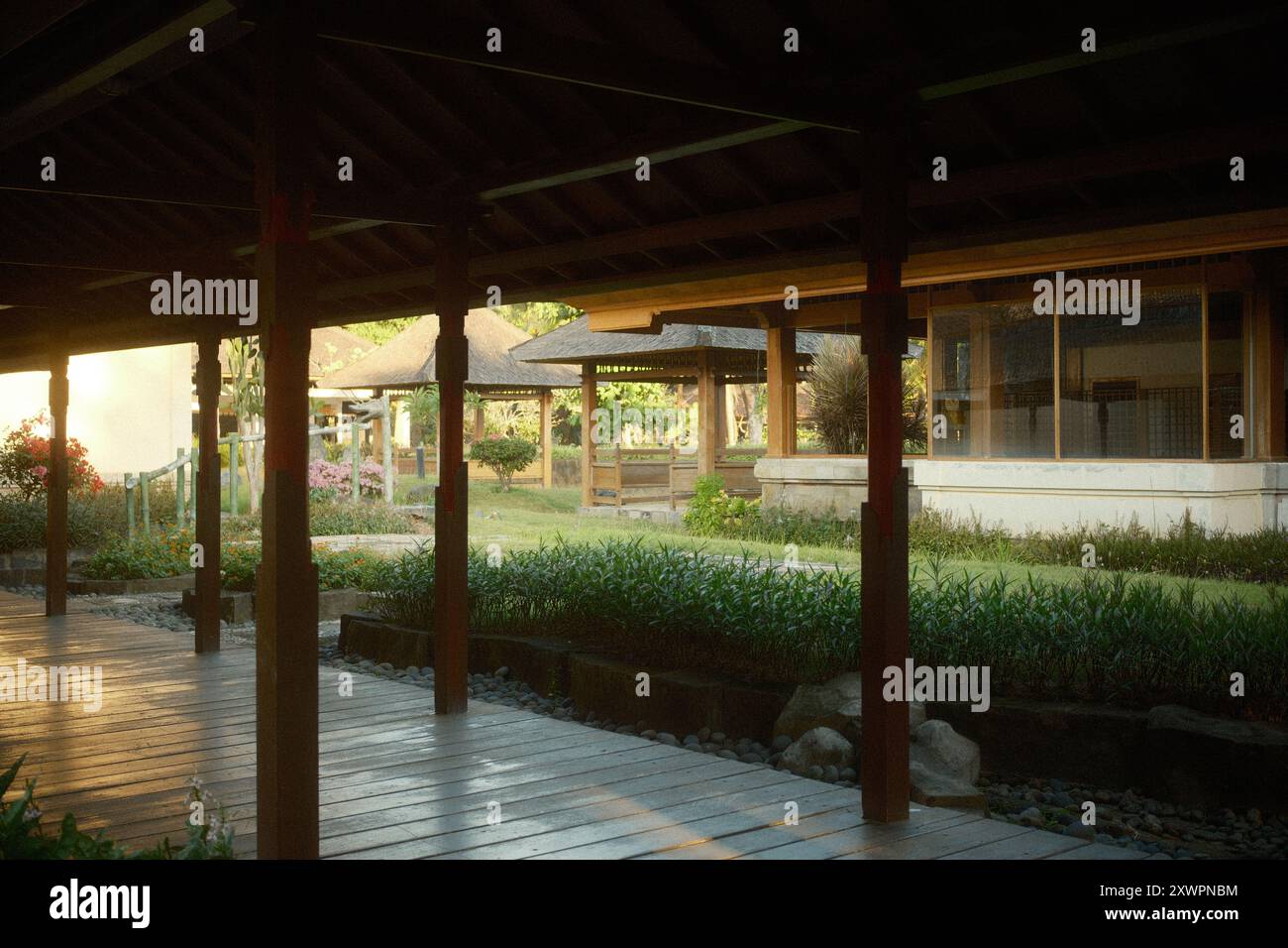 Pavilion with a wooden walkway surrounded by traditional Japanese architecture, a gazebo, and a tropical garden Stock Photo