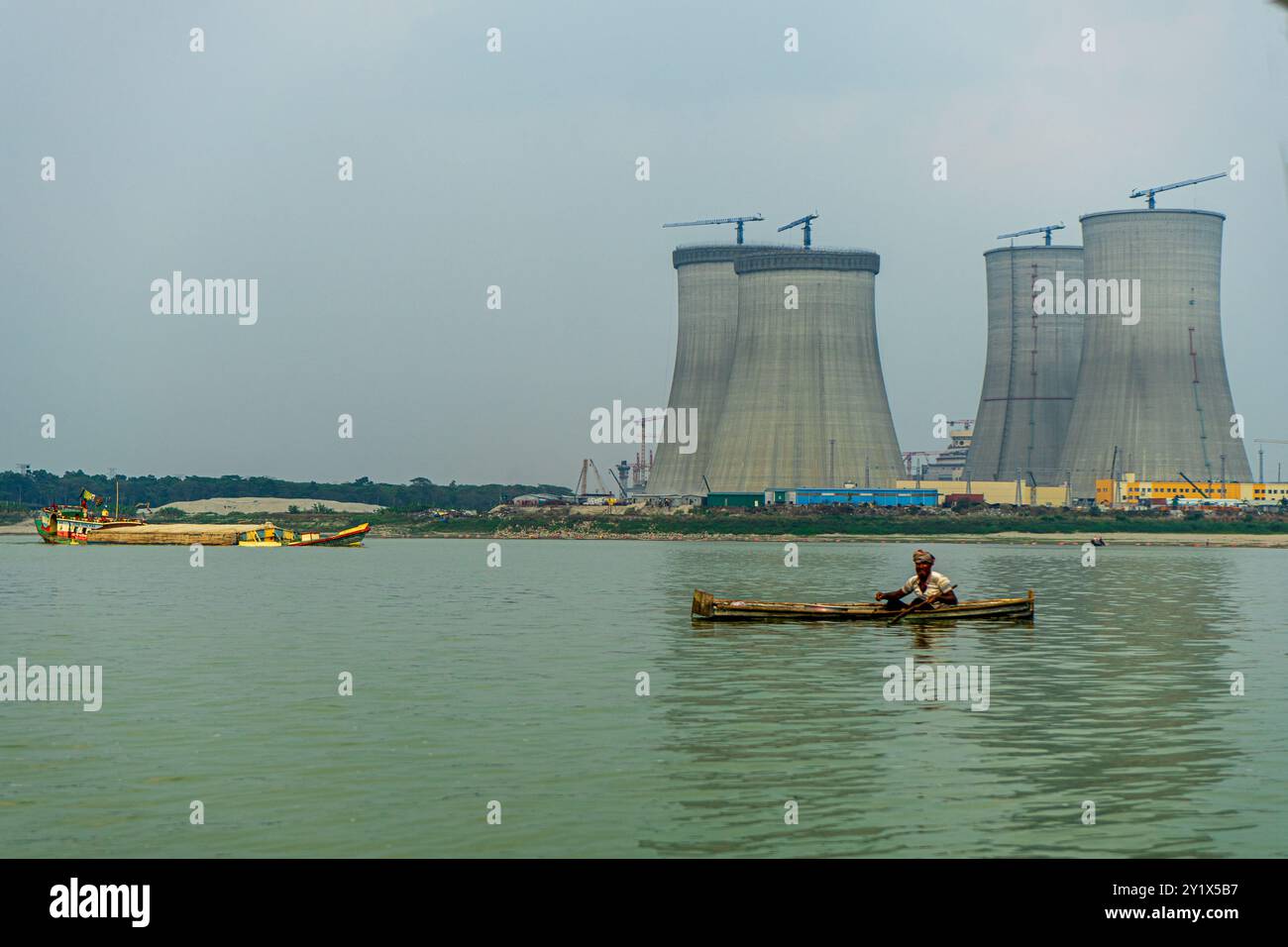 Bangladesh, Ruppur - 29.03.2024: Fisherman in boat on Ganges River, Padma with cooling towers of Rooppur Nuclear Power Plant under construction in the Stock Photo