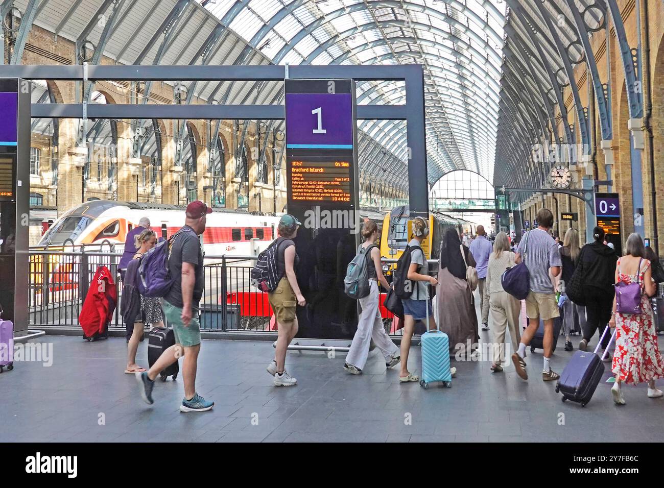 Summertime train travelers with holiday luggage walking on to platform One Kings Cross Station below historical curved roof Camden London England UK Stock Photo