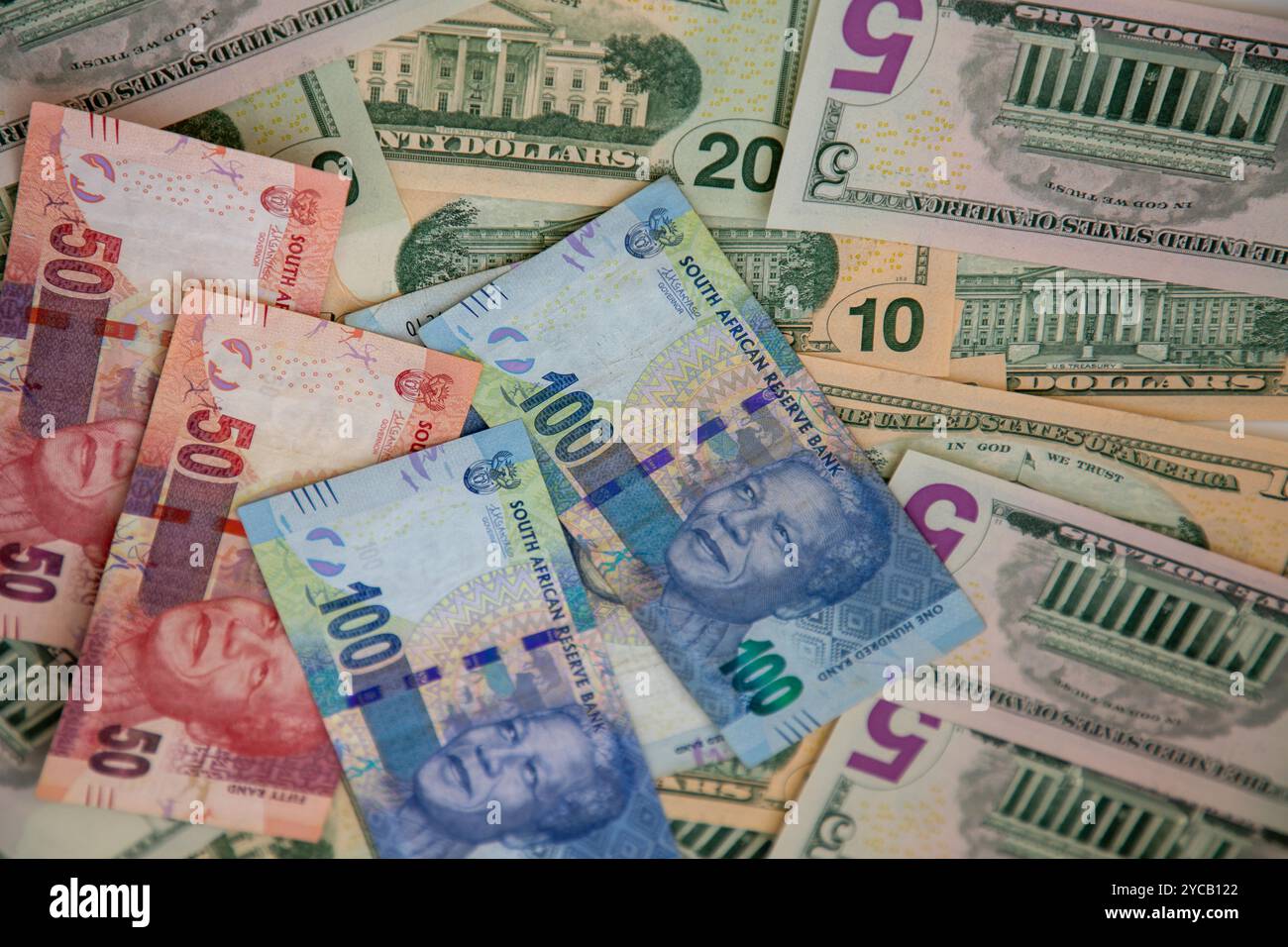 Selective focus on R50 and R100 South African currency notes with various denominations of US Dollar notes behind them. Stock Photo