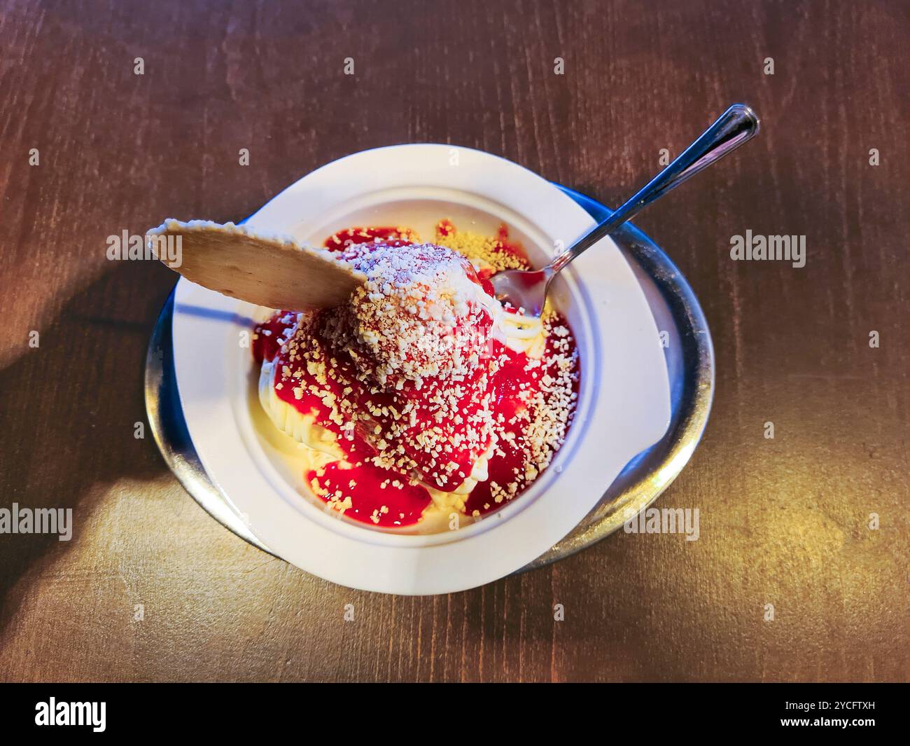 Vanilla ice cream with red strawberry sauce and white chocolate sprinkles served in a bowl as spaghetti ice cream with a round cone Stock Photo