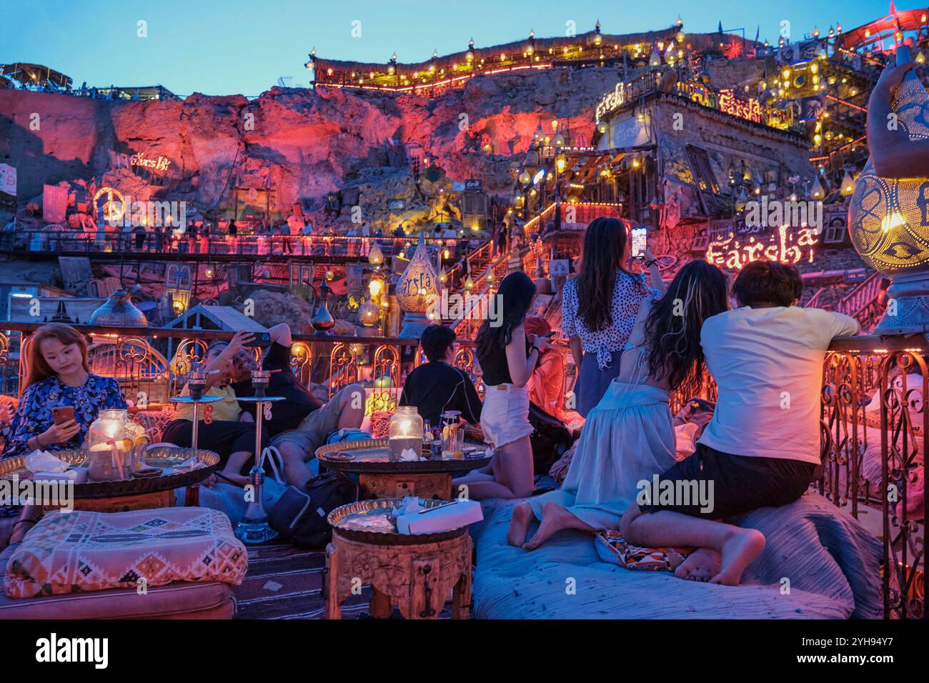 Sharm El Sheikh, Egypt - May 1, 2024: People at popular Farsha cafe take photos on their phones of night illumination of mountainside with red light, Stock Photo