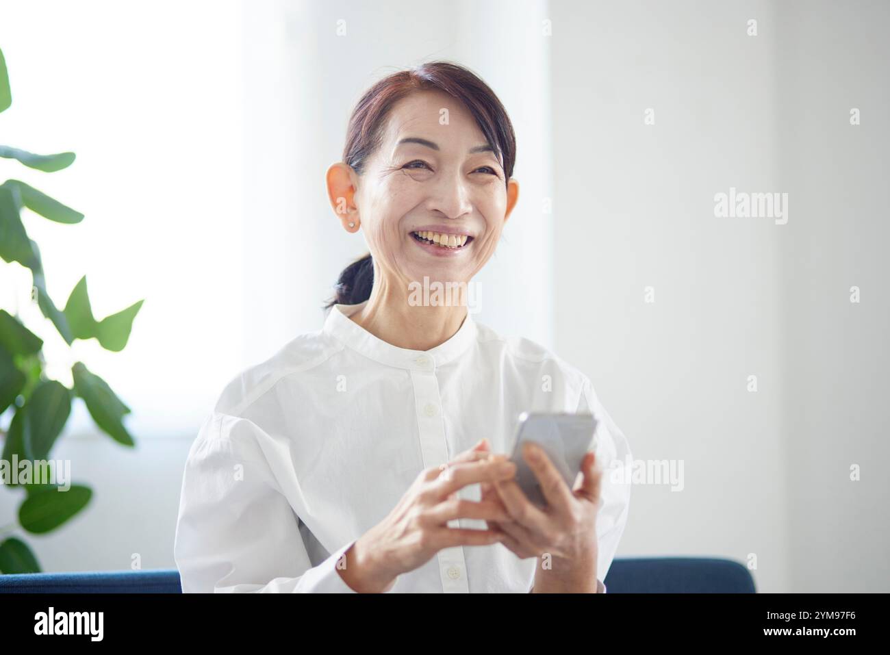 Senior Japanese woman using smartphone in living room Stock Photo