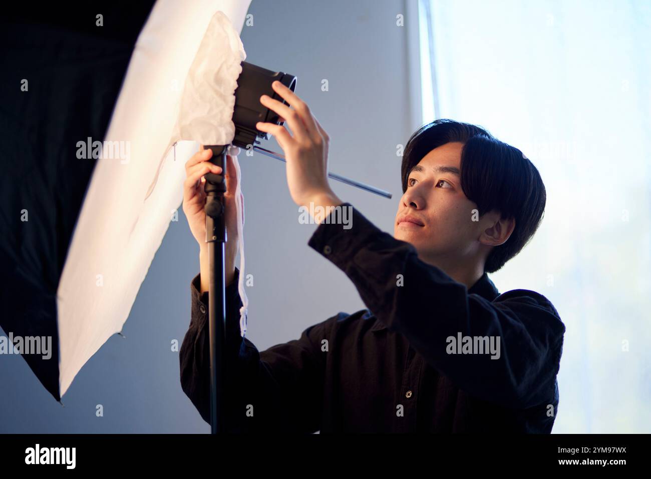 A Japanese male photographer adjusting the strobe in a photography studio. Stock Photo