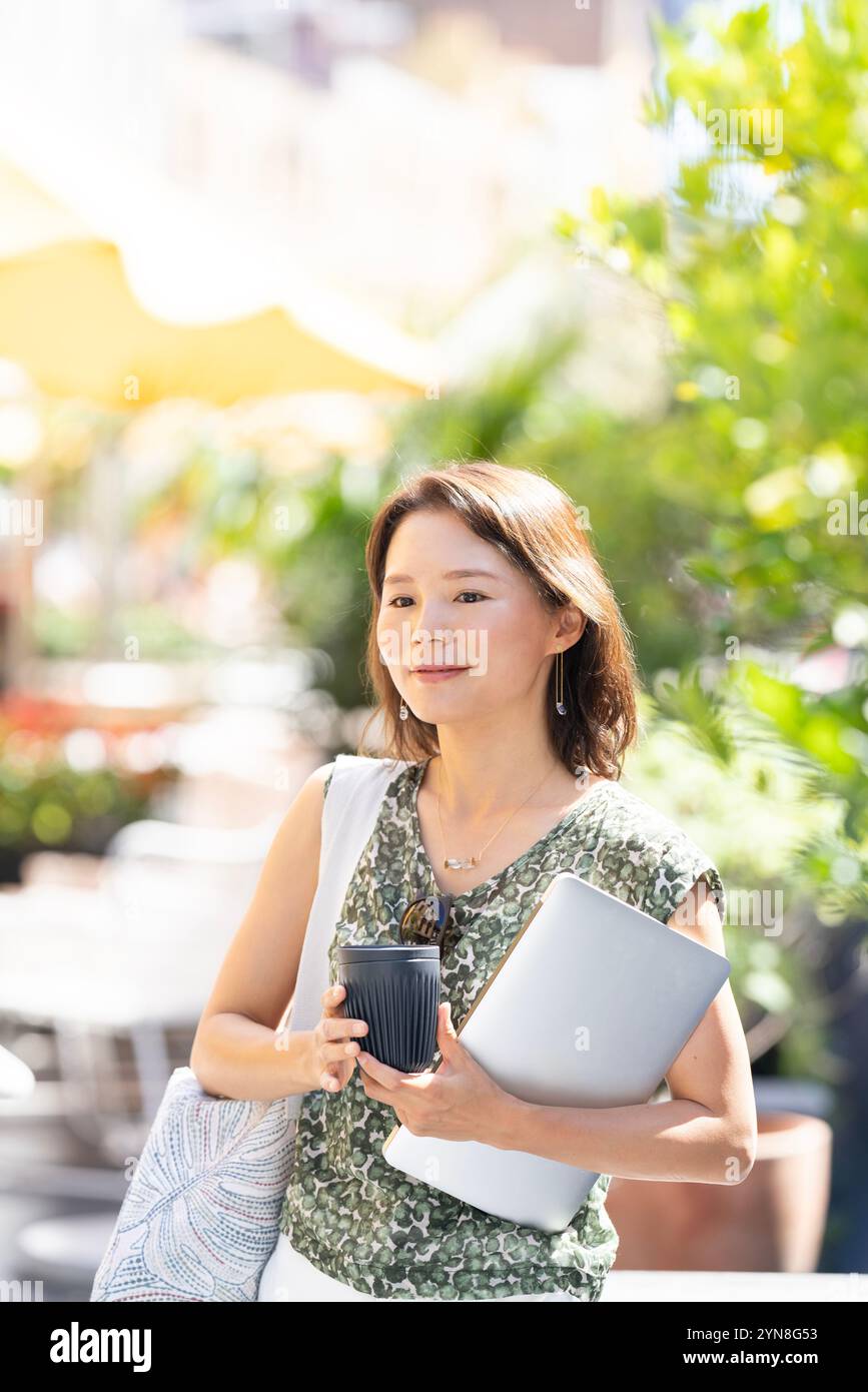 Woman walking outside with computer and coffee in hand Stock Photo