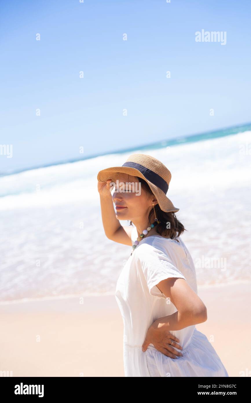 Woman walking on beach holding hat down Stock Photo