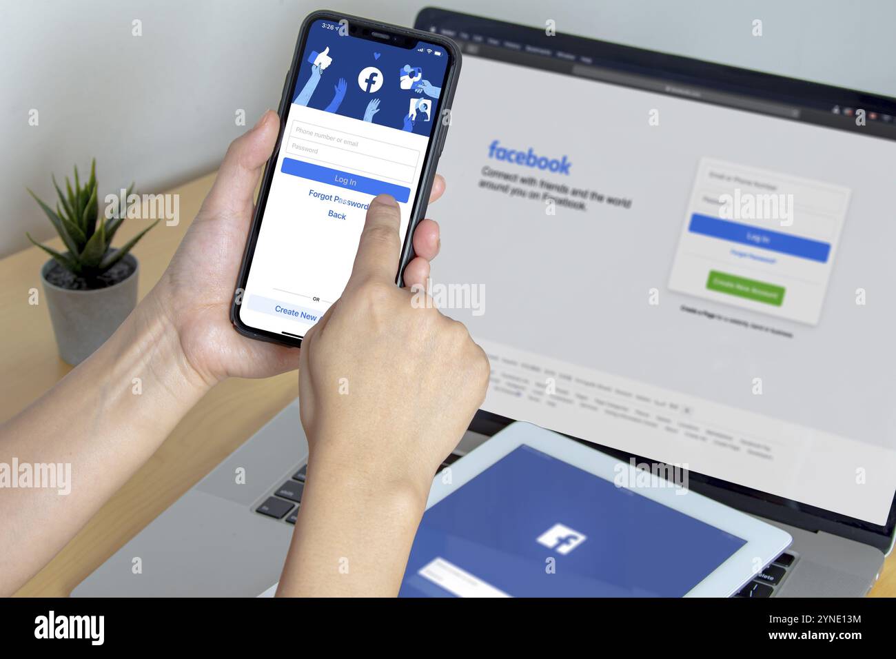 Calgary, Alberta. Canada. Nov 11 2020: A person using Facebook app on an iPhone Pro 12, iPad and a Macbook Pro on a wooden table Stock Photo