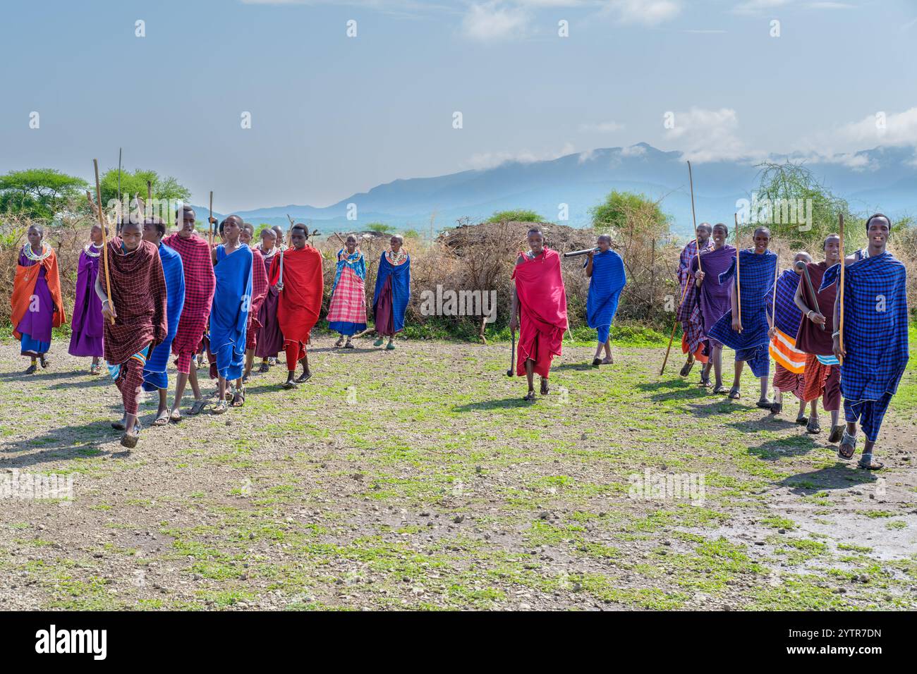 Serengeti, Tanzania - March 7, 2017: Maasai men and women in traditional garb at the edge of their village with mountains in the background Stock Photo