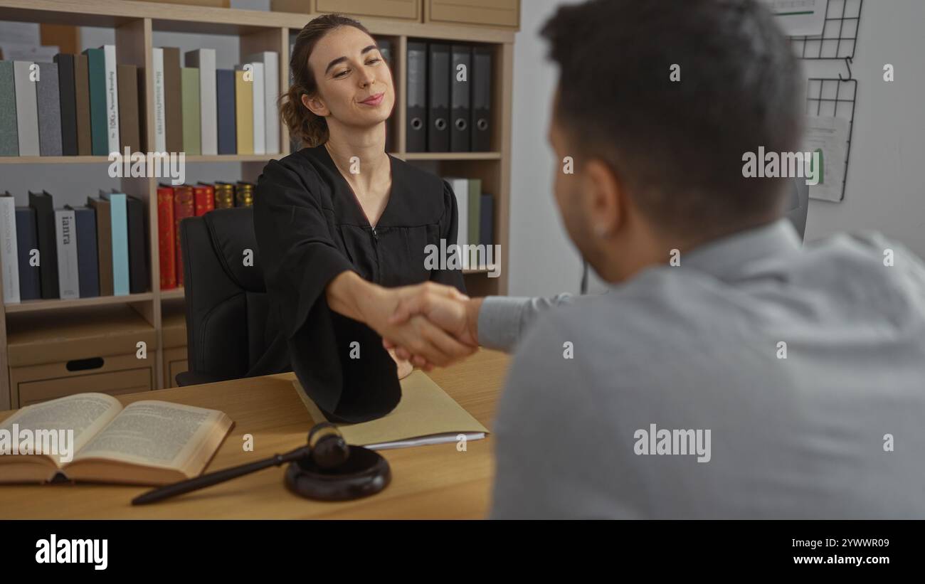 Woman judge shaking hands with man client in office while seated at desk with law book and gavel Stock Photo