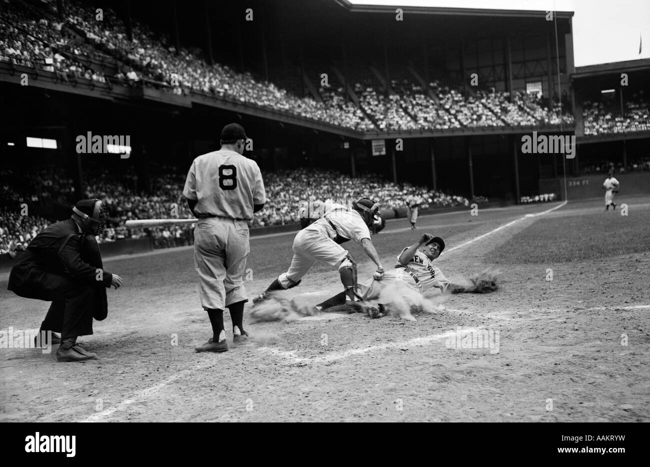 1950s BASEBALL GAME UMPIRE AND BATTER WATCH AS CATCHER PROTECTS HOME PLATE WHILE RUNNER SLIDES IN TRYING TO STEAL HOME Stock Photo