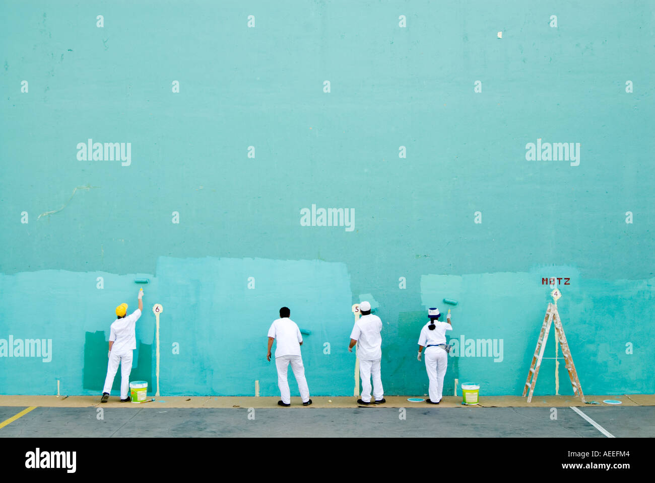 Team of workers painting large blank wall turquoise for game of pelota, Spain Stock Photo