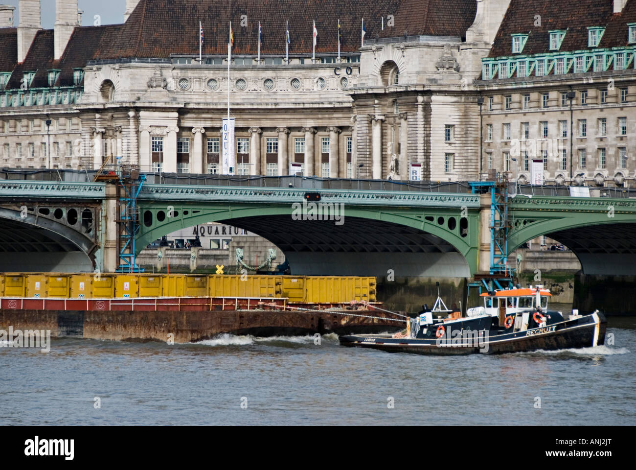 A tug towing cargo barges passes under Westminster Bridge, London, UK. The old County Hall building in the background Stock Photo